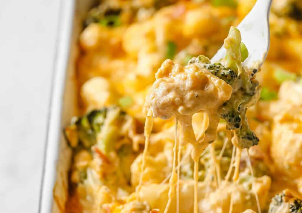 A fork with cheesy broccoli on it being pulled up from a loaded broccoli cauliflower casserole.