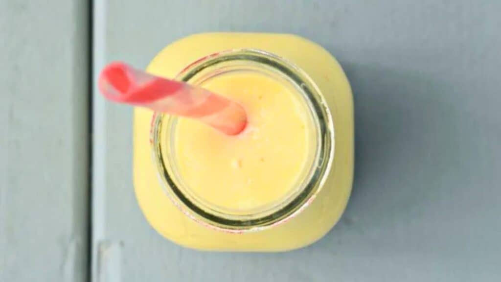 Image shows an overhead closeup image of a Mango Lassi in a glass jar with a straw in it.