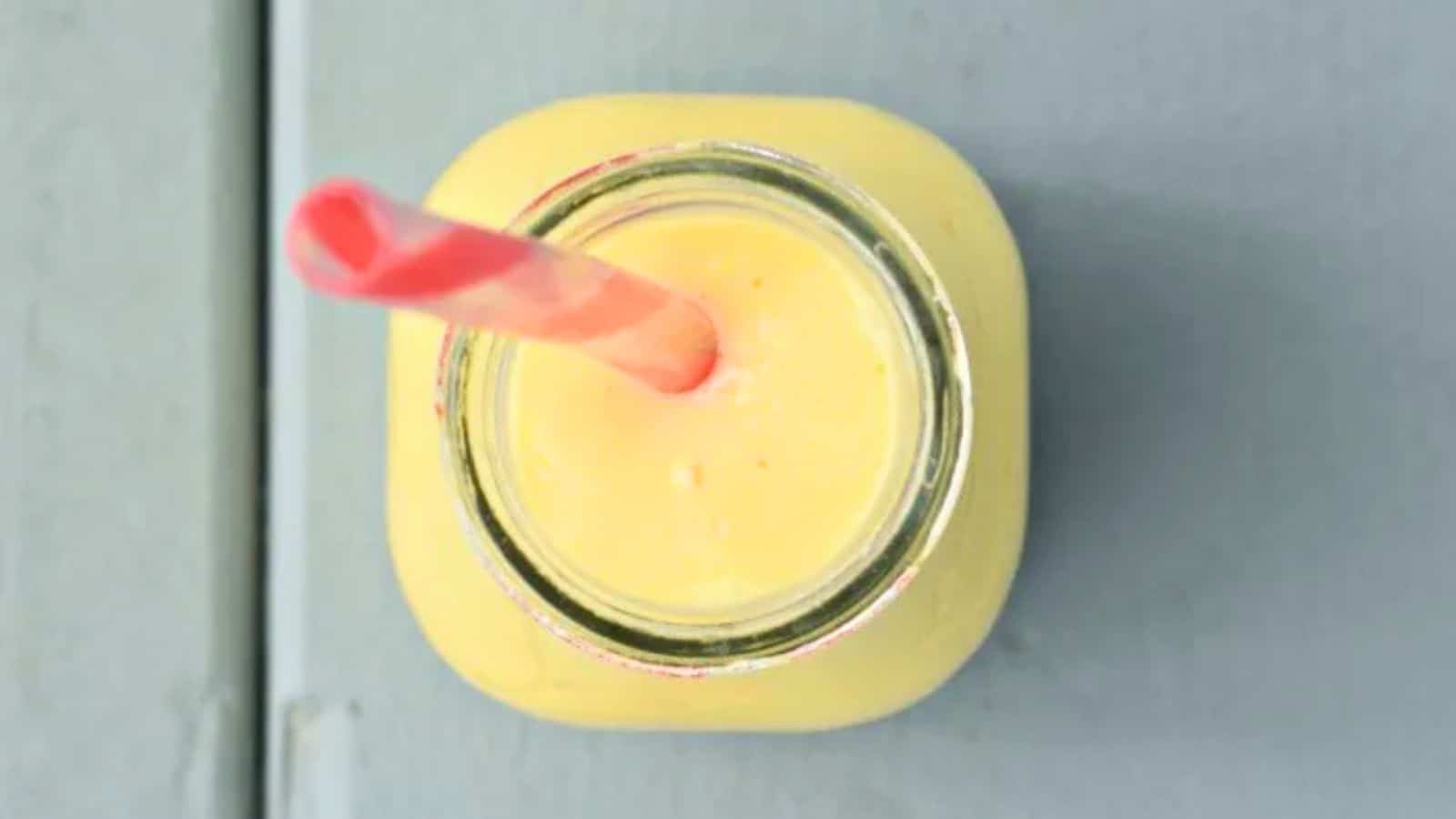 Image shows an overhead closeup image of a Mango Lassi in a glass jar with a straw in it.