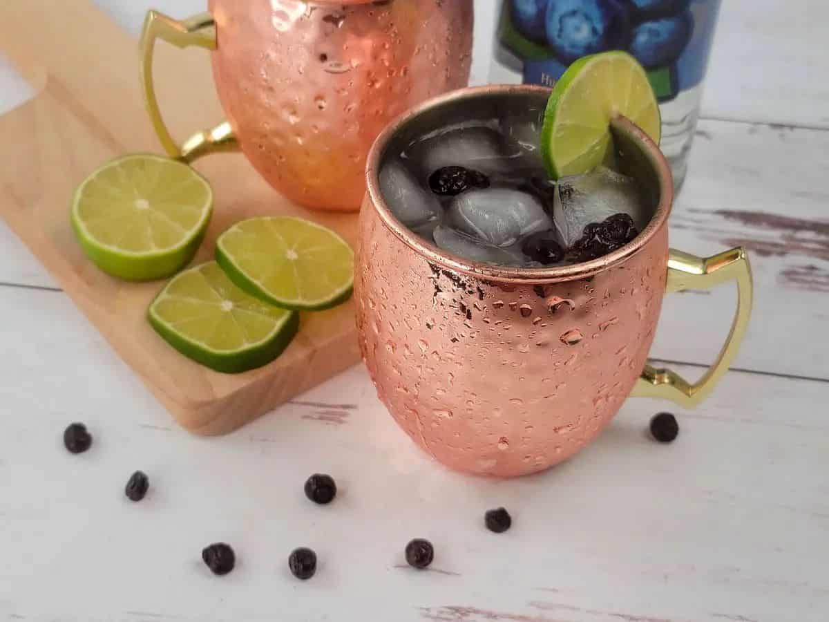 A copper mug surrounded by sliced limes and huckleberries.