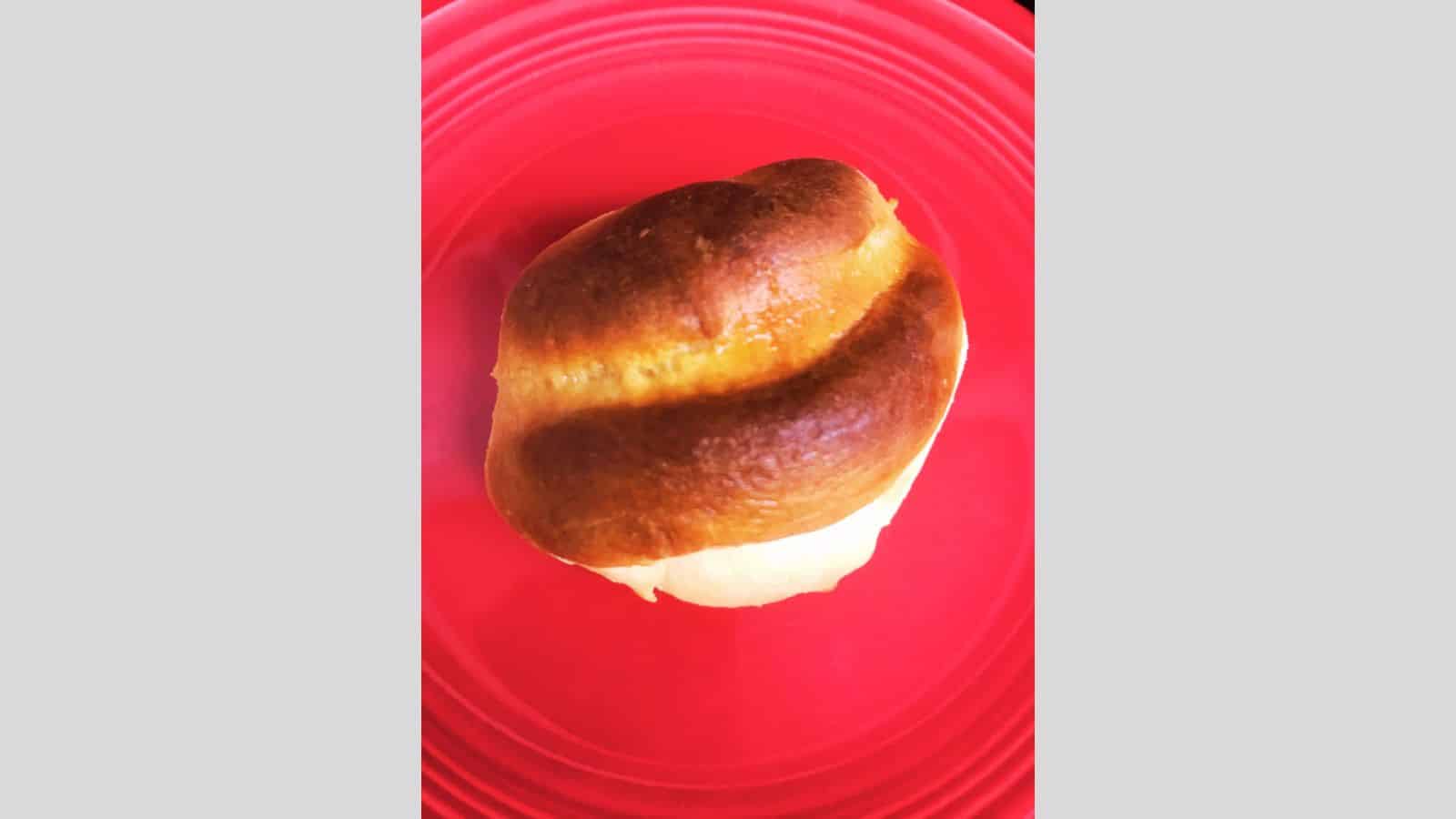 A single bread roll, the star of many cherished bread recipes, rests on a vibrant red plate.