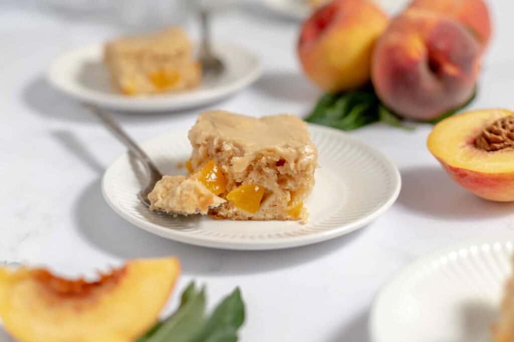 A slice of peach cake with a bite of cake on a fork surrounded by peaches.