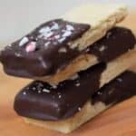 Image shows a stack of four Peppermint Shortbread Cookies on a wooden table.