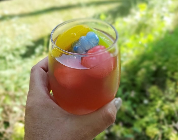 Image shows a hand holding a glass of pomegranate lemonade with green grass in the background.