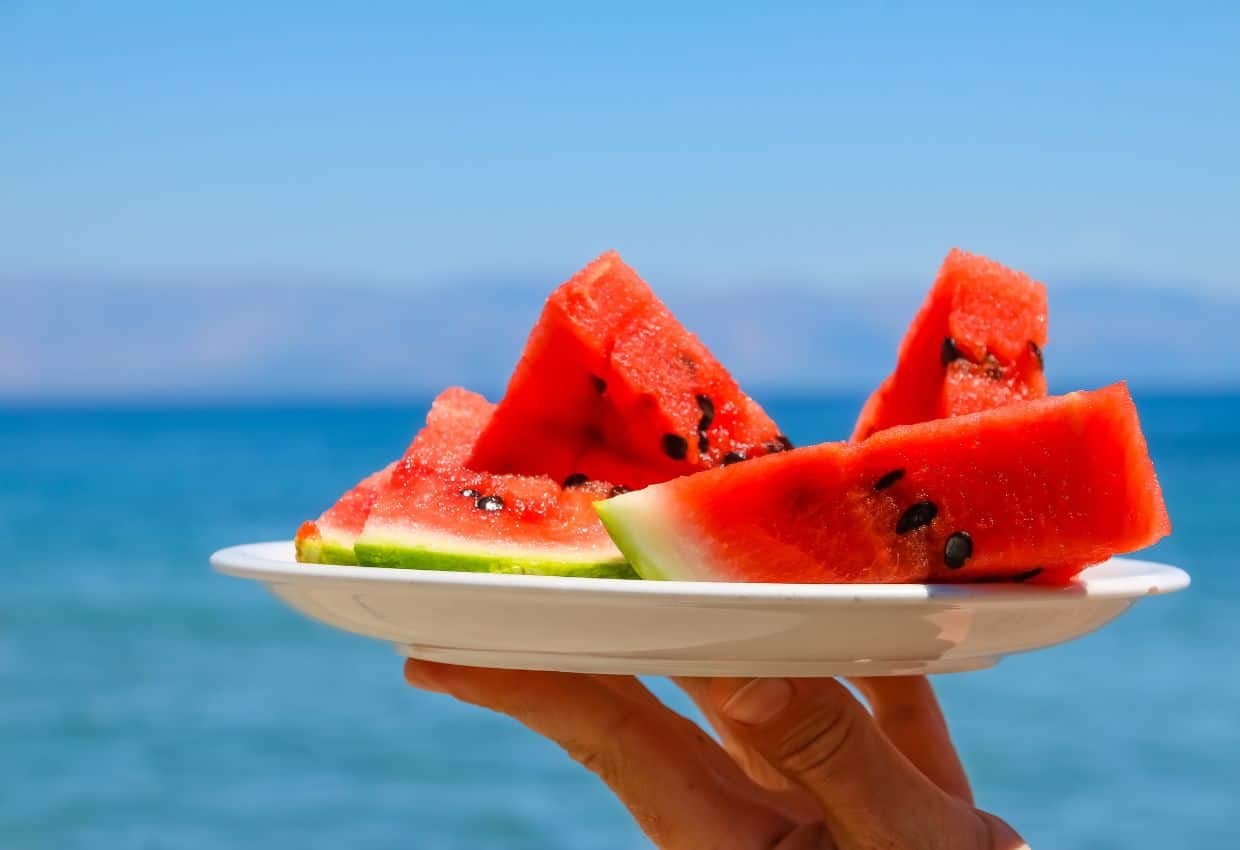Image shows Perfect watermelon slices on a plate with the ocean in the background.