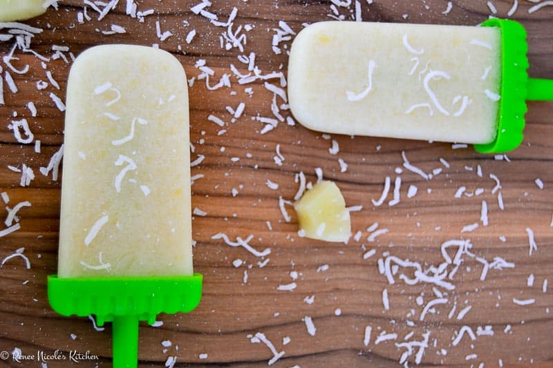 Two pina colada popsicles on a wooden background.
