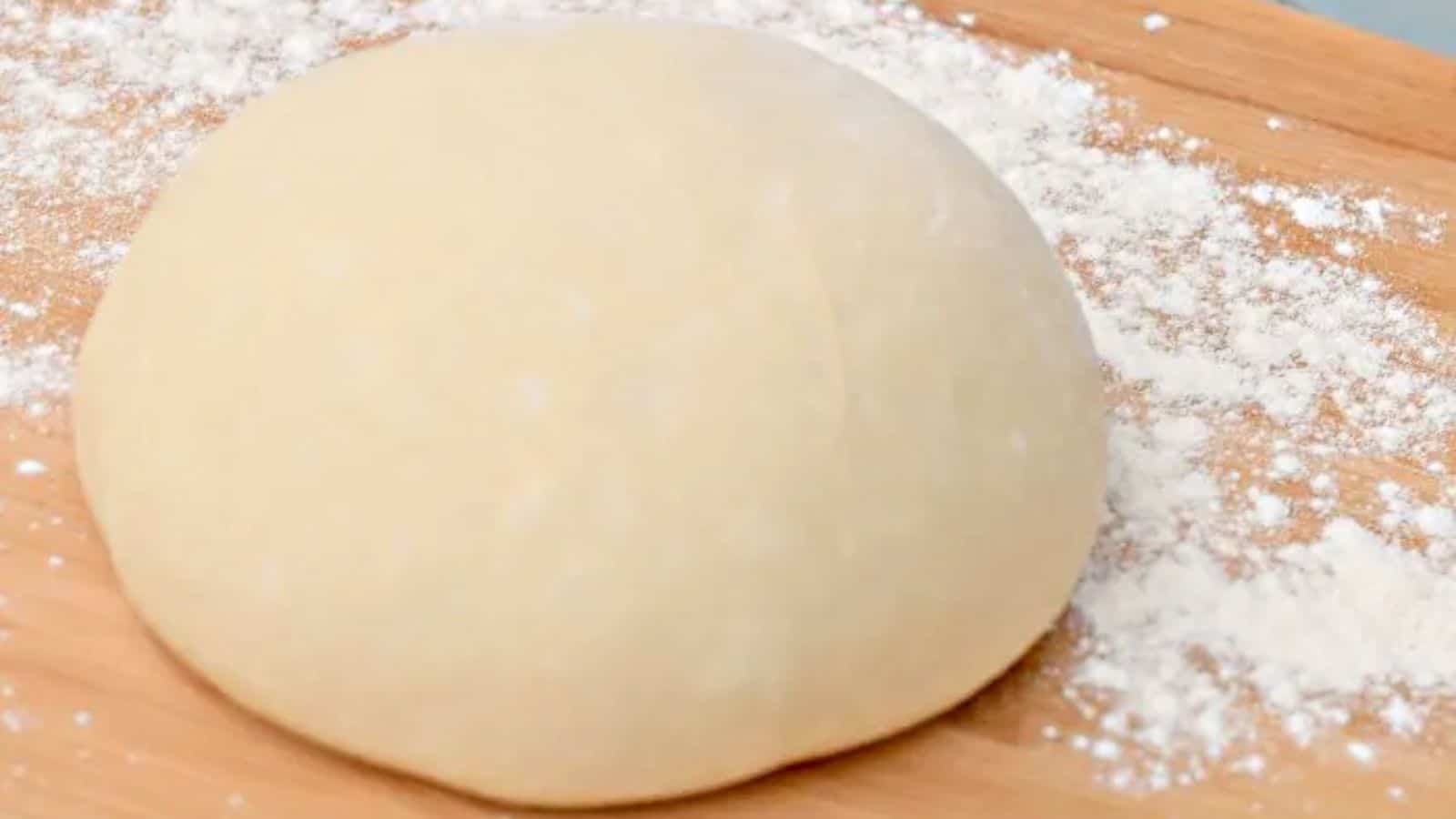 Image shows a round of Pizza Dough on a wooden board coated with flour.