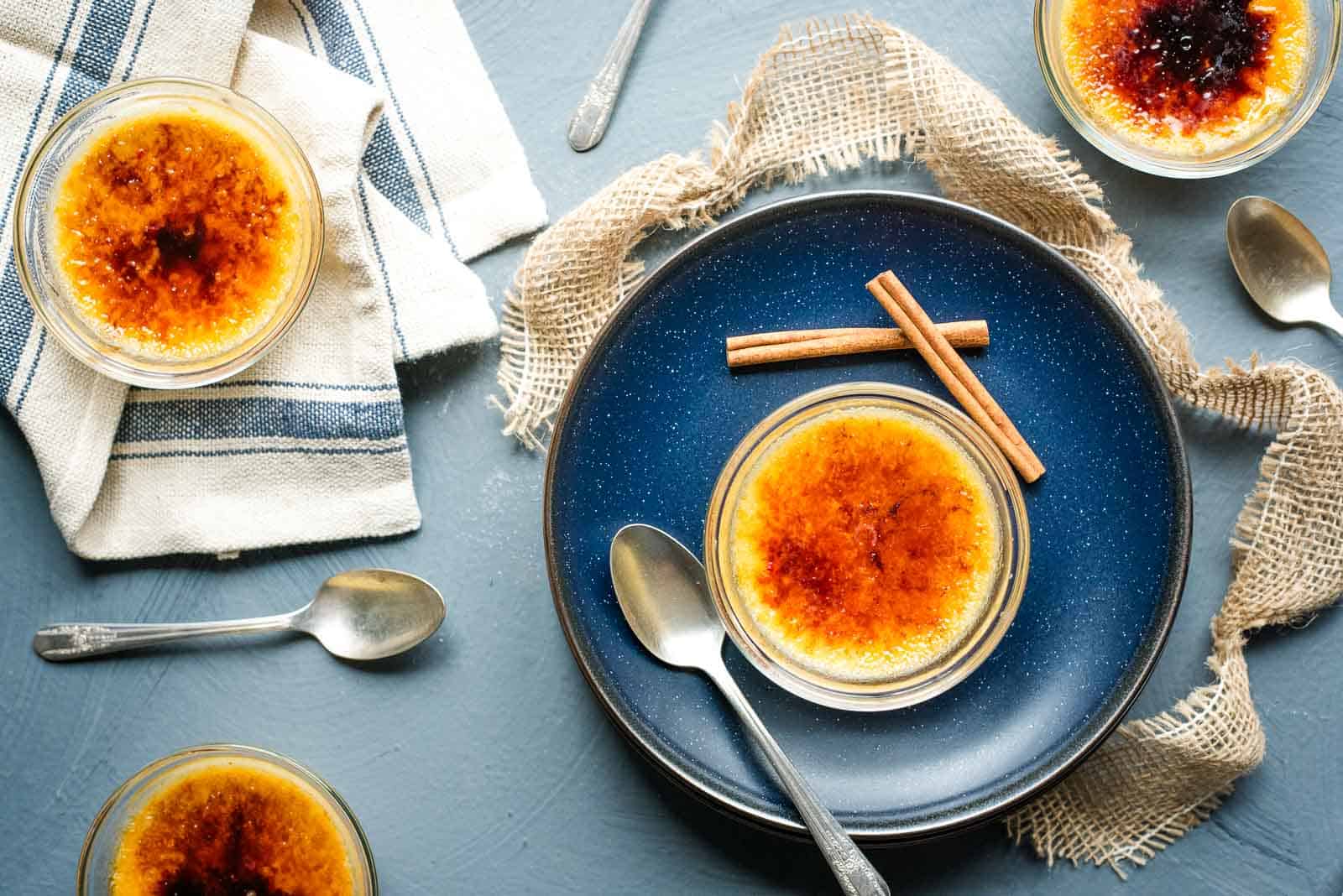 Pumpkin spice creme brulee on a blue plate with a spoon and cinnamon sticks.