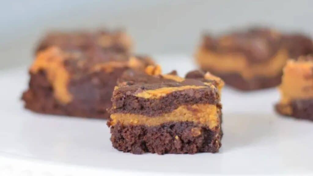 Image shows Pumpkin Swirl Brownies sitting on a white tray with one in focus and the others blurred behind it.