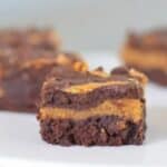 Image shows Pumpkin Swirl Brownies sitting on a white tray with one in focus and the others blurred behind it.