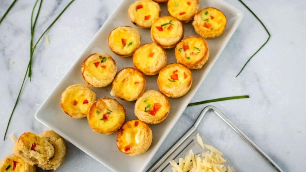 Mini Swiss cheese quiches on a white platter.