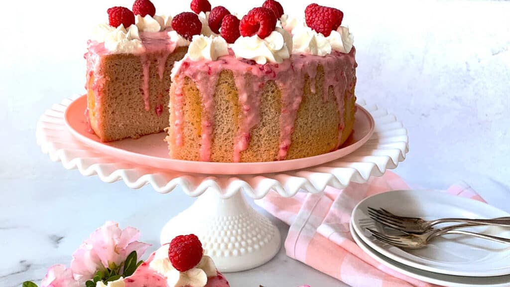 Raspberry cake on a white stand with plates and napkins.