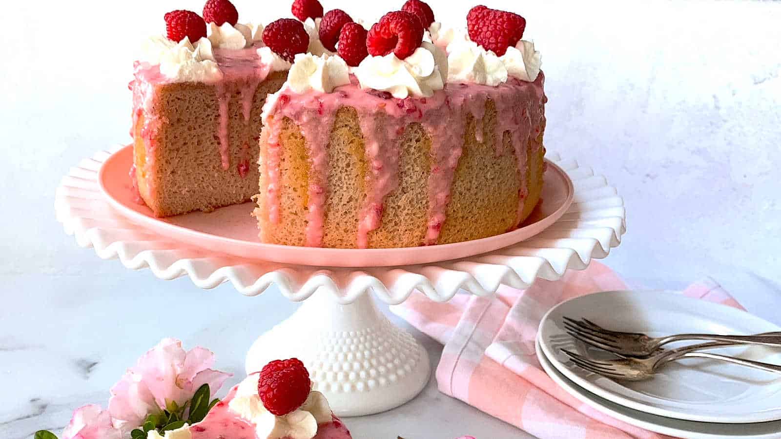 Raspberry cake on a white stand with plates and napkins.