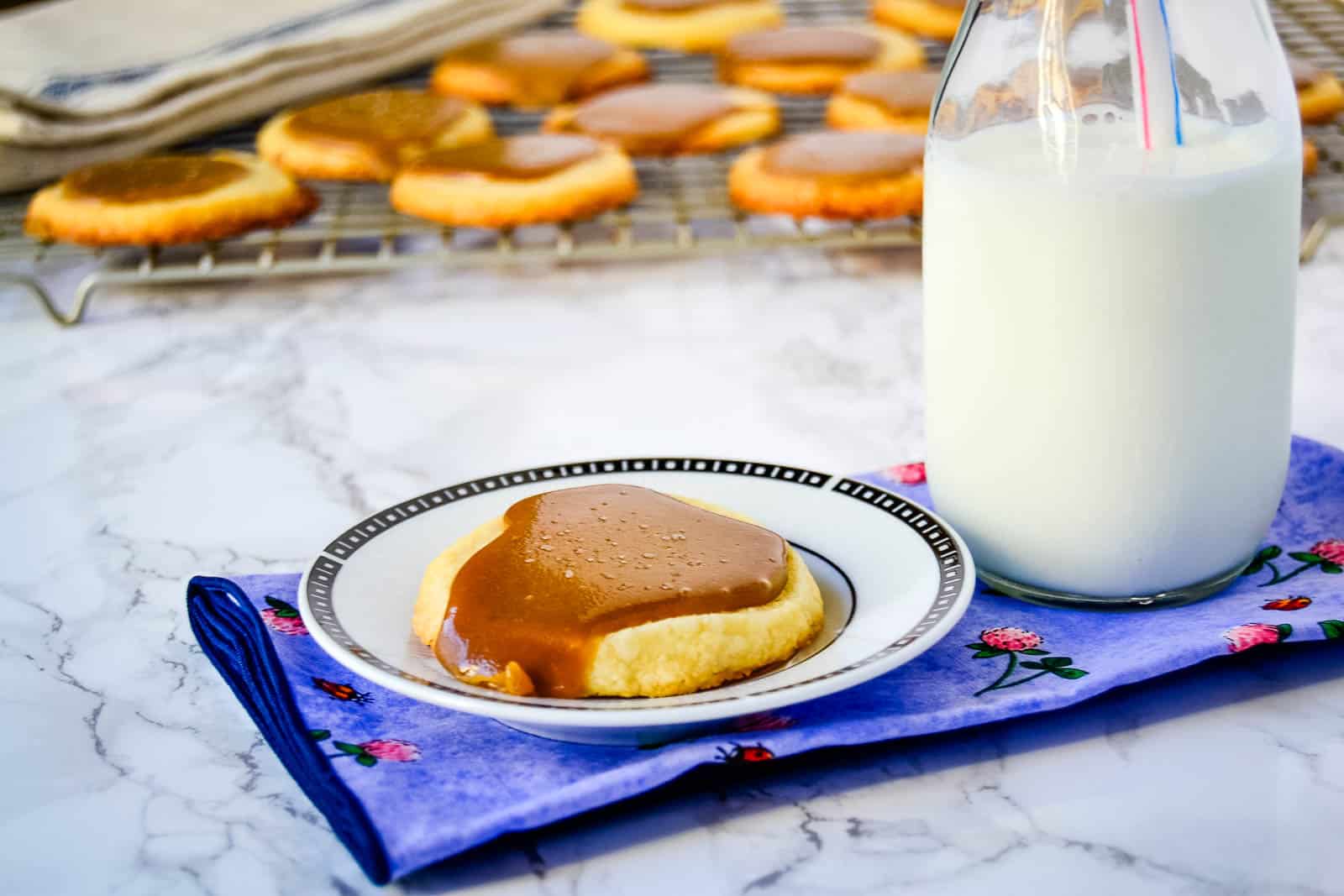 One Salted Bourbon Caramel Shortbread Cookies cookie on a white plate next to a bottle of milk.