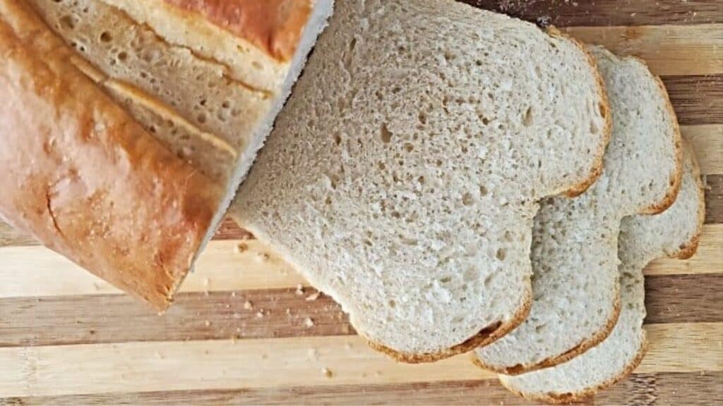 Image shows an overhead shot of a loaf of homemade Sandwich Bread partially sliced on a wooden board.