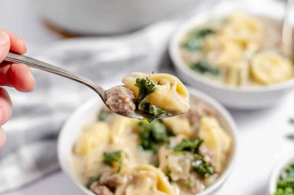 Sausage and tortellini soup in a bowl with a spoonful of soup. 