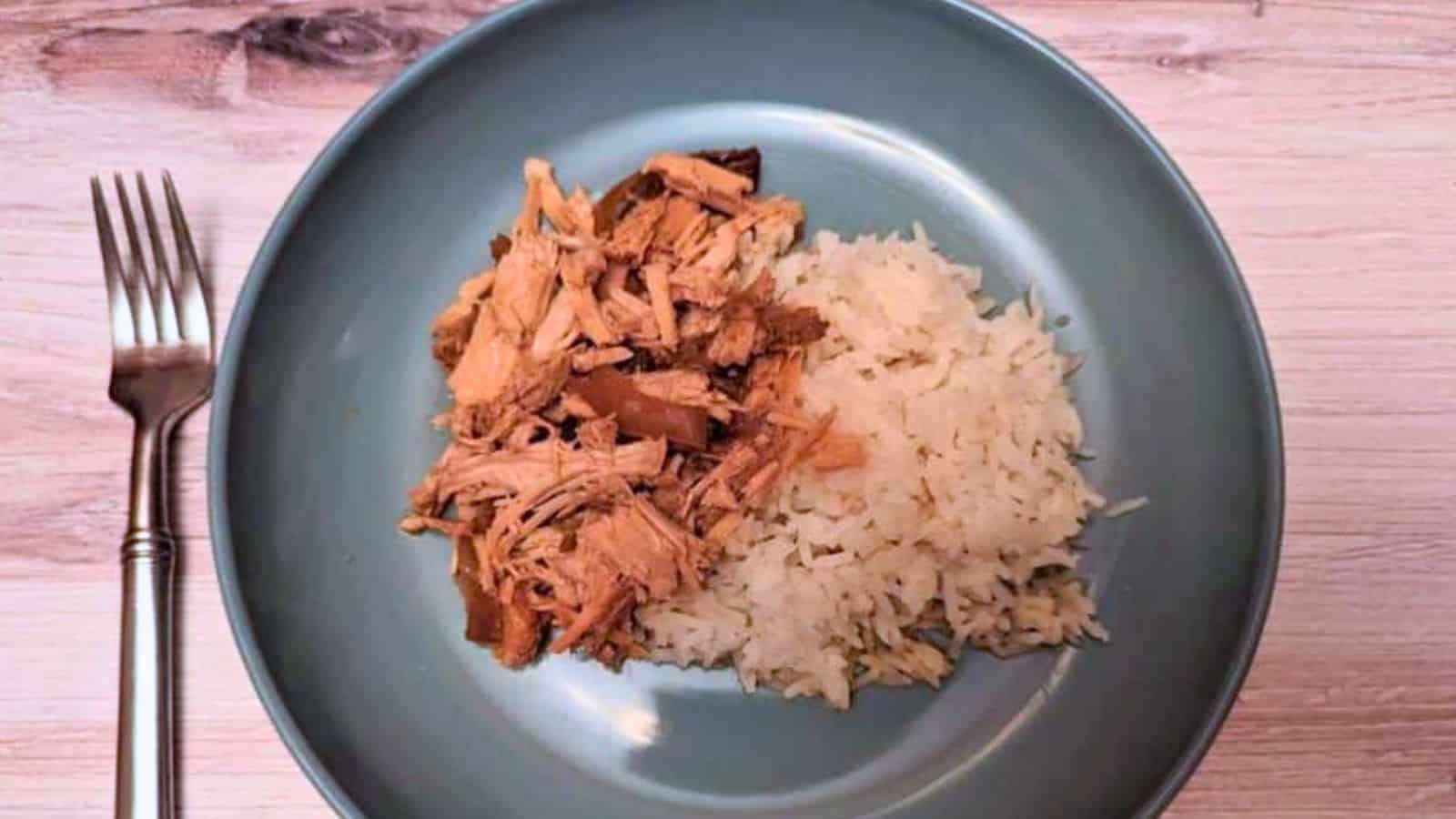 Image shows an overhead shot of Slow Cooker Garlic Roast Pork on a blue plate served with rice.