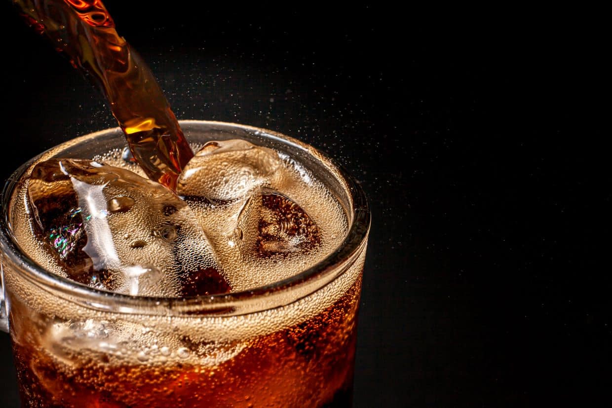 Cola being poured into glass with ice cubes.