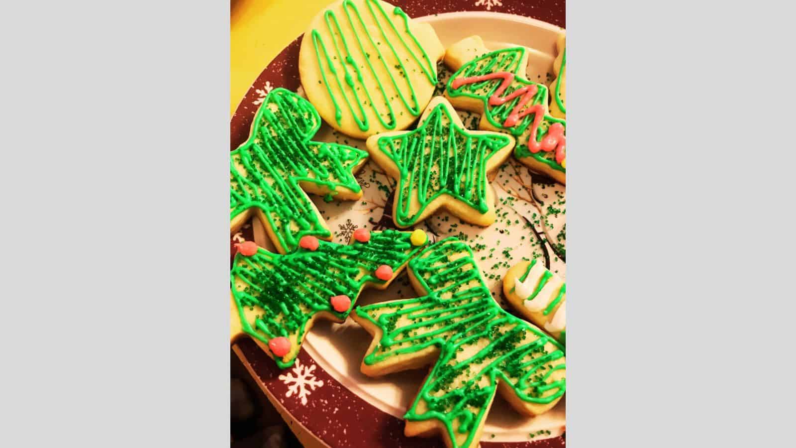 Sugar cookies shaped like trees, ribbons, and stars on Christmas plate.