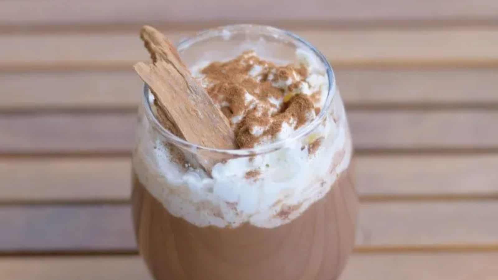 Image shows a Spicy Cinnamon Mocha in a clear glass with a cinnamon stick in the foam.