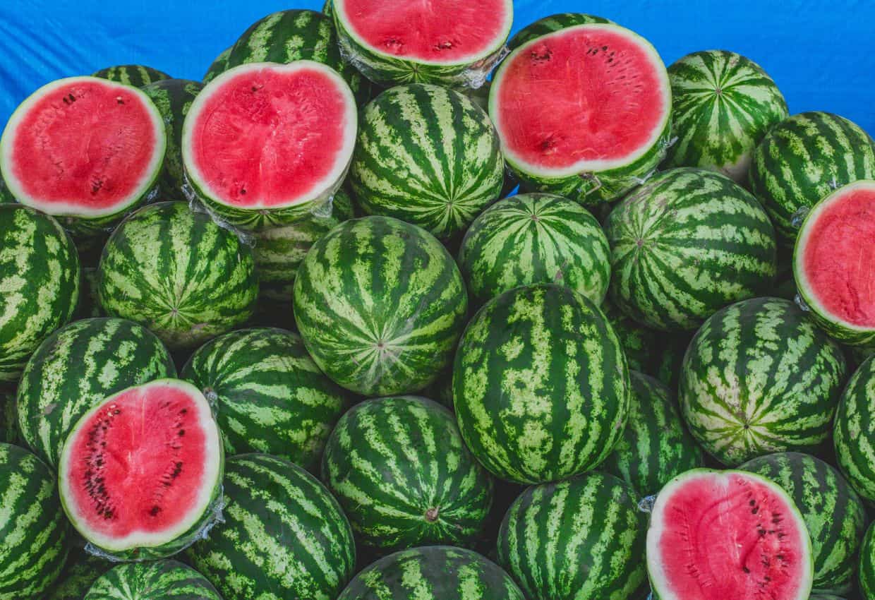 Image shows a Stack of whole and cut in half watermelons.