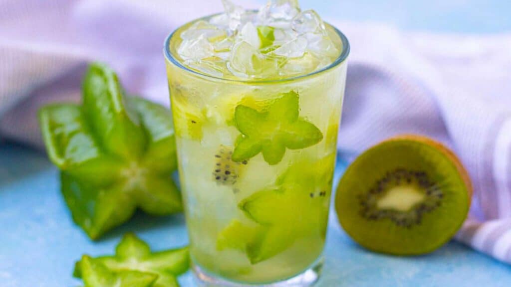 An enticing glass of Starbucks Kiwi Starfruit Refresher, garnished with slices of kiwi and starfruit, showcasing its vibrant green color and refreshing appeal.
