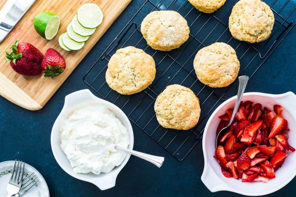 Set up to assemble strawberry shortcake: homemade biscuits, whipped cream, lime macerated strawberries.