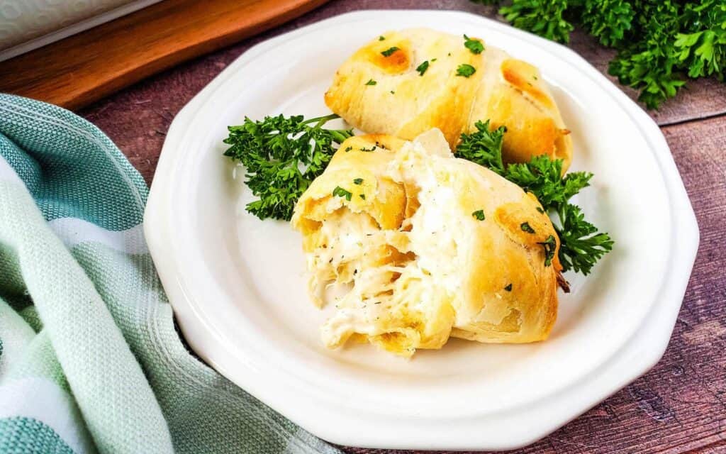 Front view of 2 stuffed chicken Crescent rolls on a white plate garnished with parsley.