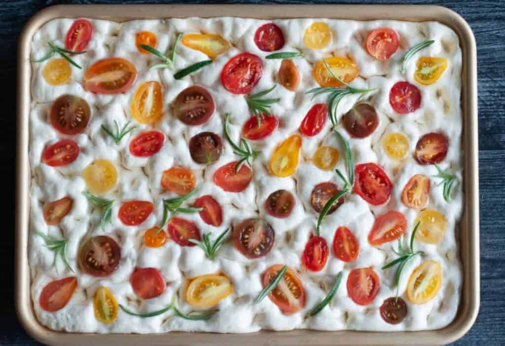 Focaccia bread dough topped with olive oil, sliced tomatoes, and herbs. 
