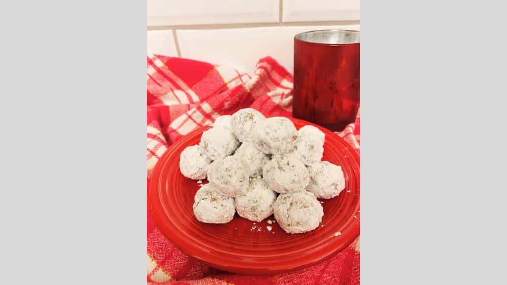 Rum balls stacked on red plate with red glass in background.