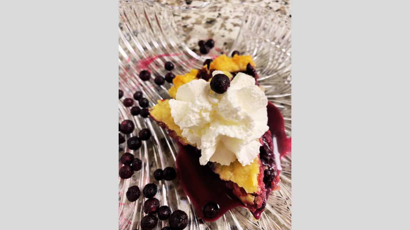 Slice of blueberry pie with whipped cream on glass plate.