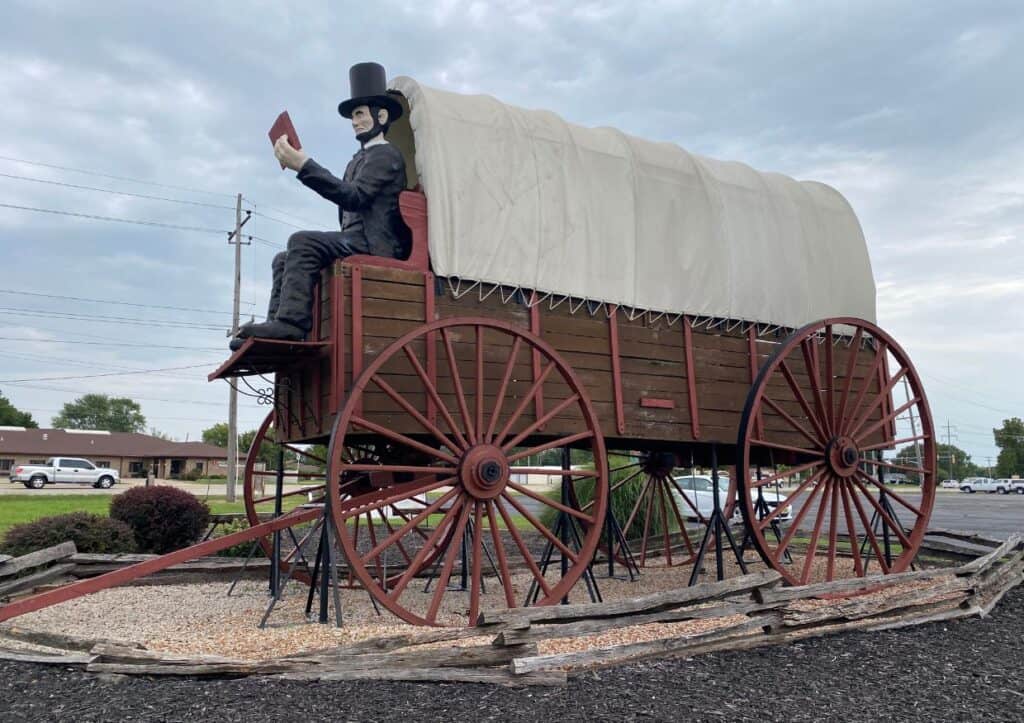 A statue of Abraham Lincoln riding a large covered wagon at a roadside attraction in Illinois.