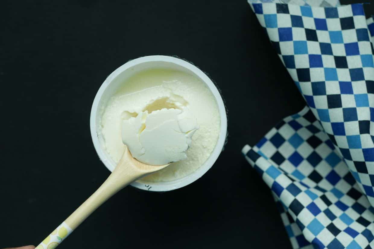 Top view of wooden spoon scooping yogurt from container.