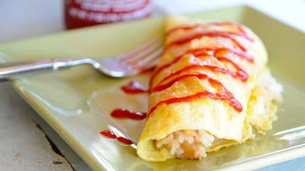 Omelet on a plate stuffed with adobe fried rice and topped with hot sauce.