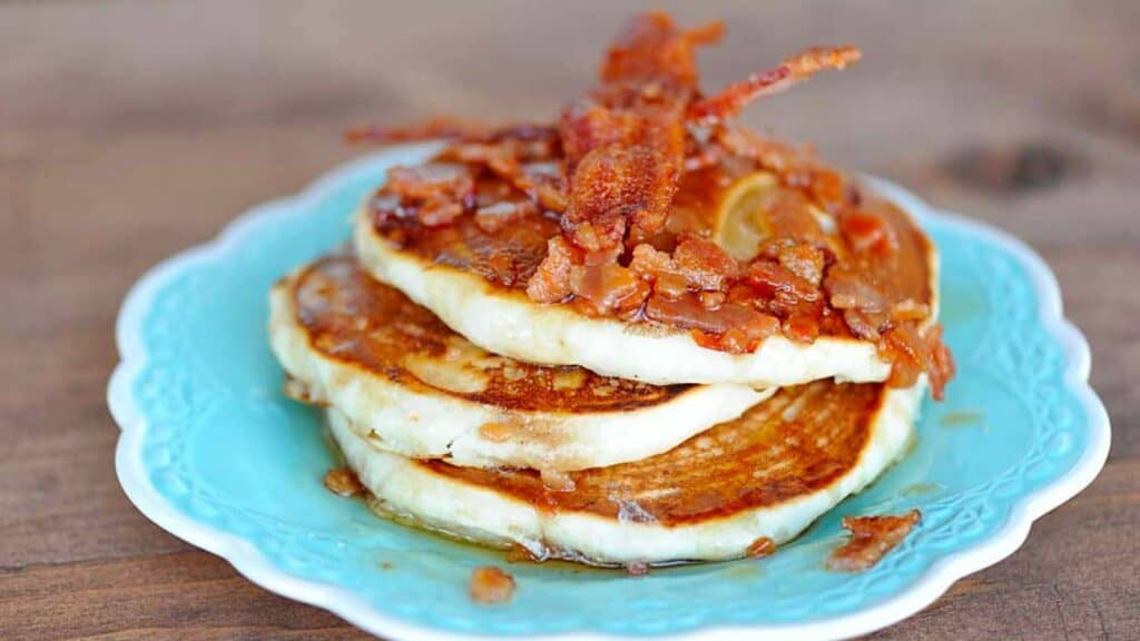 Stack of pancakes topped with bacon maple syrup.