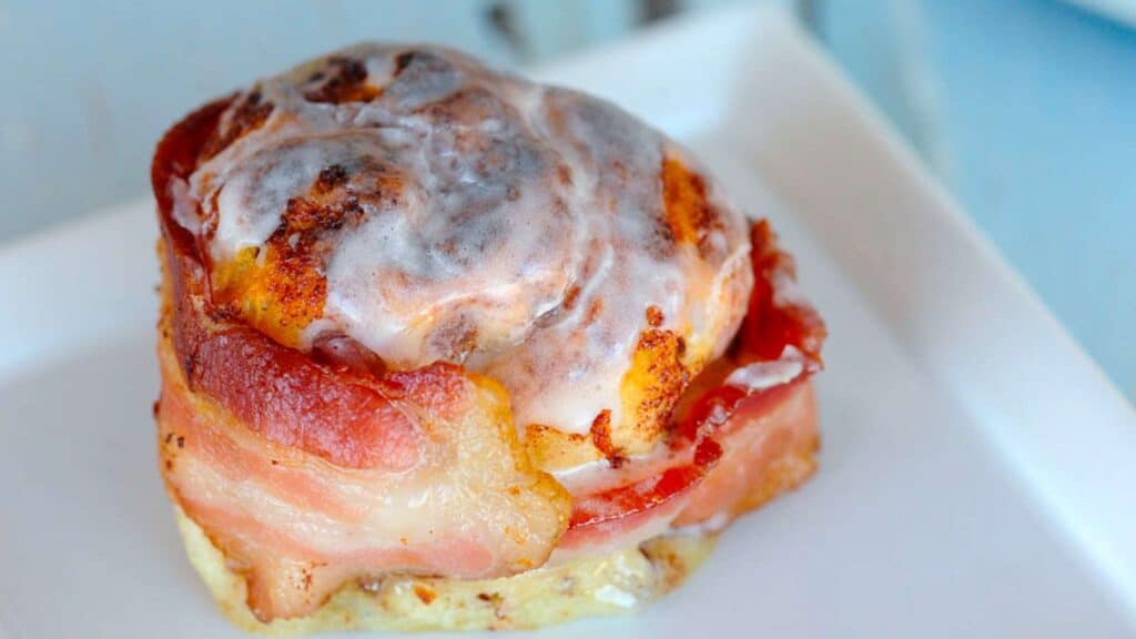 Bacon wrapped around a cinnamon roll on a plate.