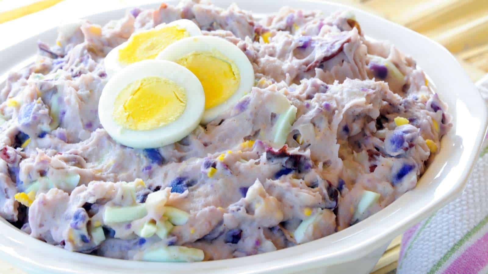Bowl of purple potato salad with sliced hard-boiled-eggs on top.