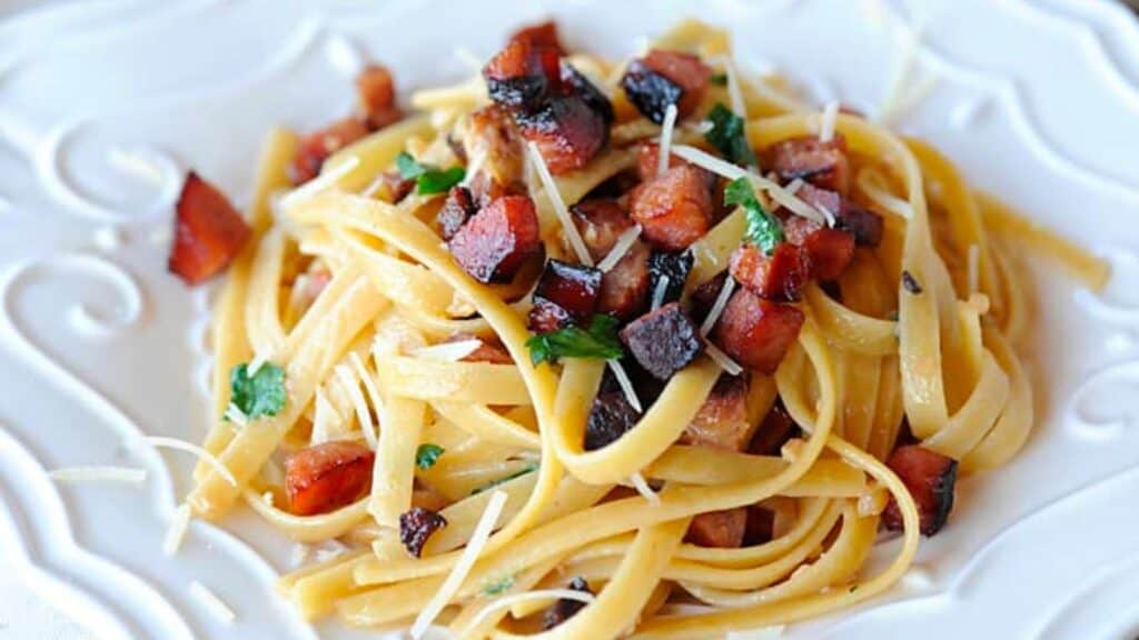 Plate of fettuccine Alfredo topped with smoked sausage and veggies.