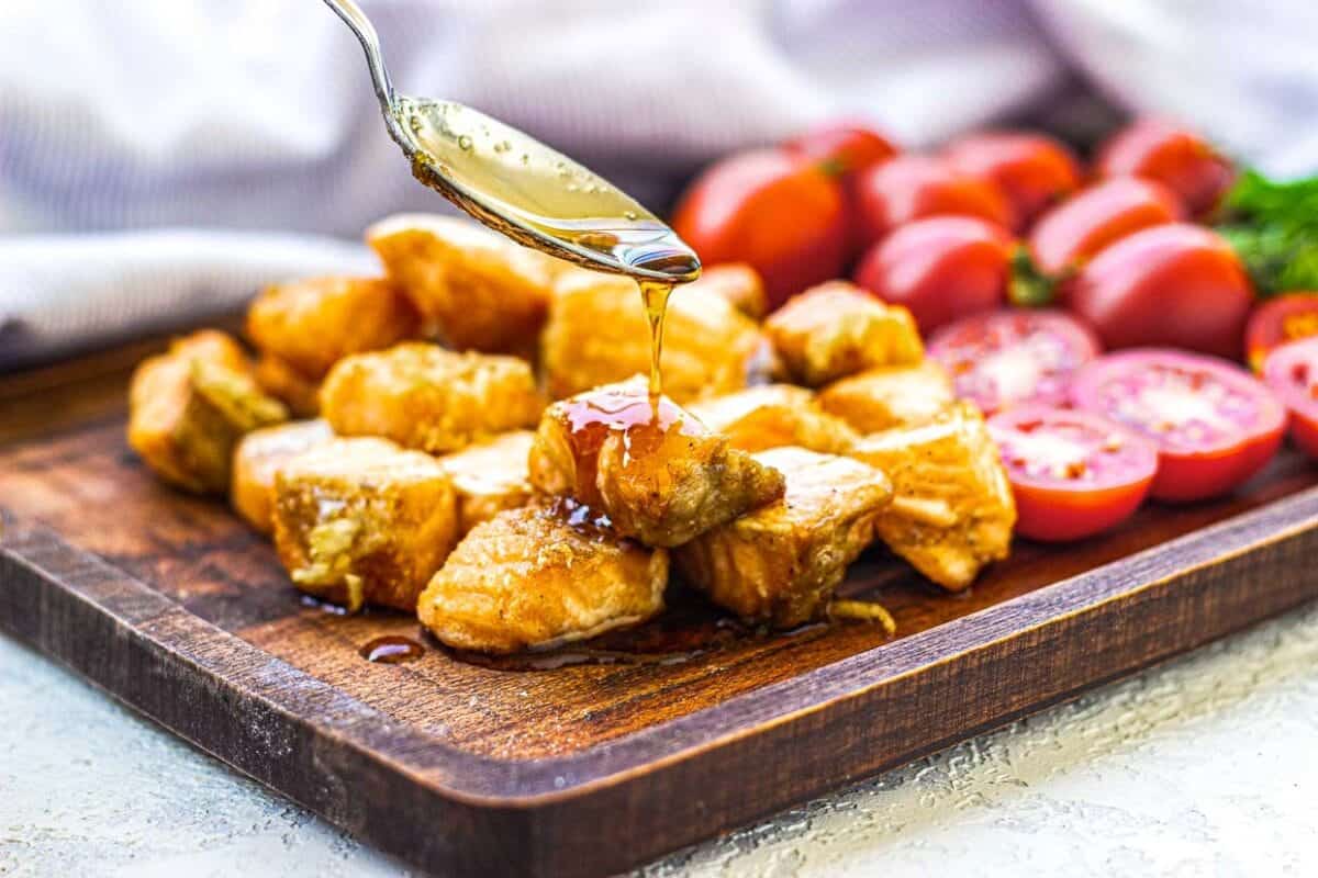 Drizzling sauce over crispy salmon bites on a cutting board.