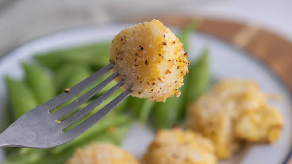 Closeup of an air fryer scallop on a fork with a plate of scallops in the background.