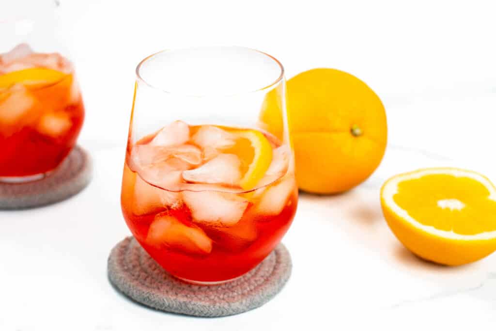 An aperol spritz on grey coasters on a white background with oranges.