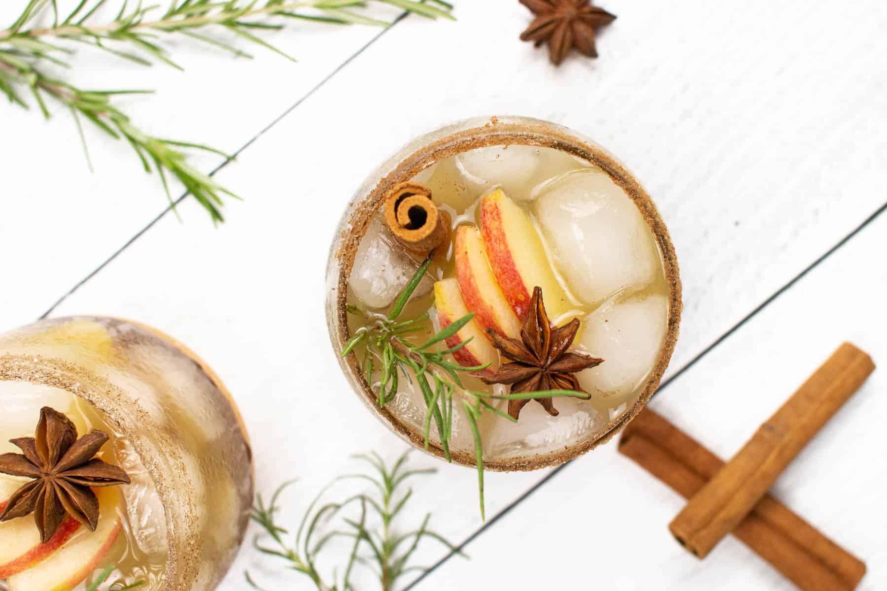 An inviting glass of apple cider sangria placed near rosemary and cinnamon sticks.