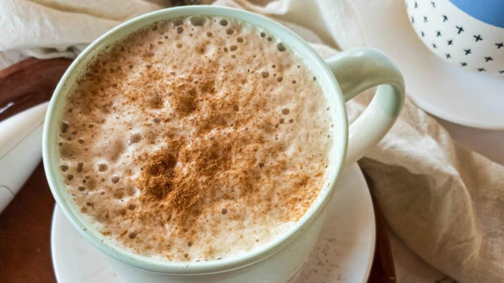 Ashwagandha latte with cinnamon dust in ceramic mug on a saucer.