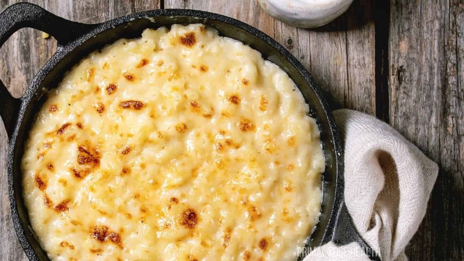 A picture of baked cauliflower mac and cheese in cast iron skillet on wooden table.