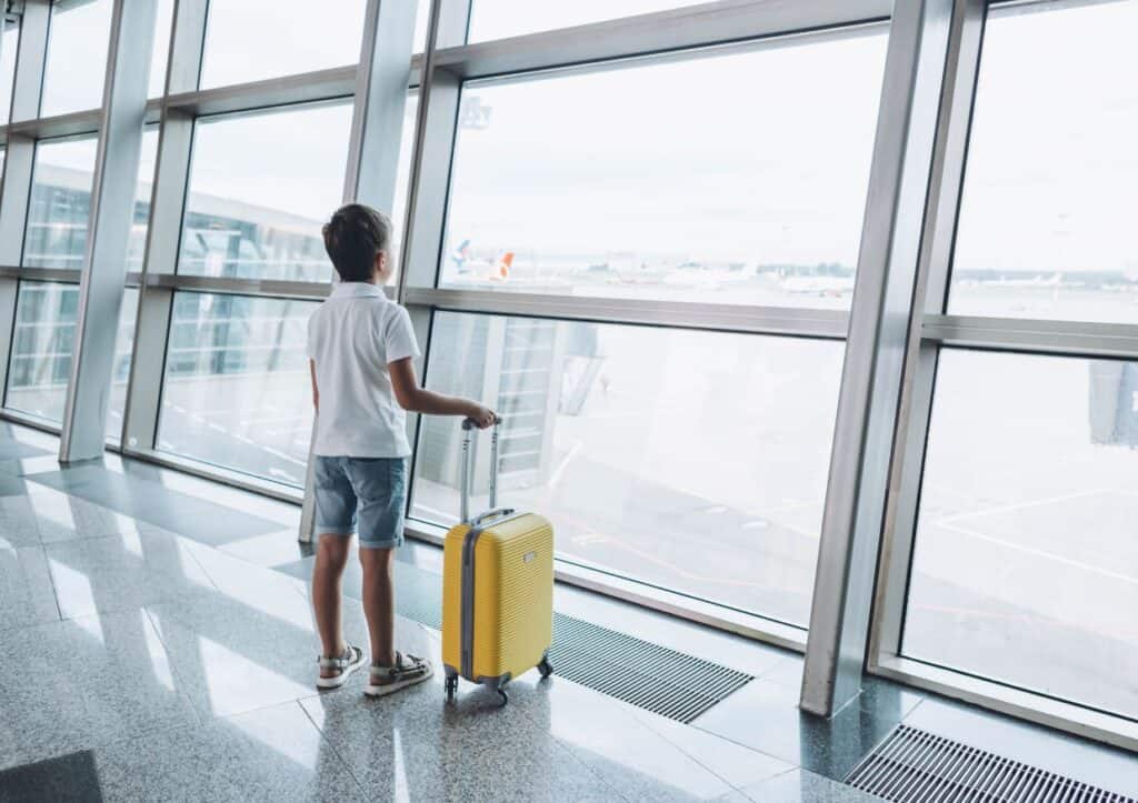 Boy standing with yellow carry-on luggage at airport.