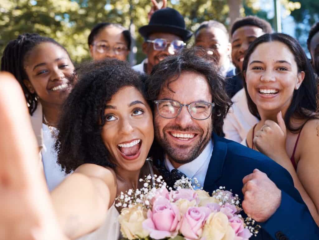 Bride and groom taking wedding selfie with friends.