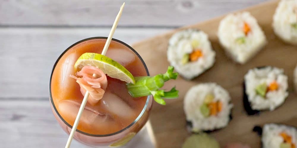 Top view of a bloody mary with celery and pickled ginger and sushi in the background.
