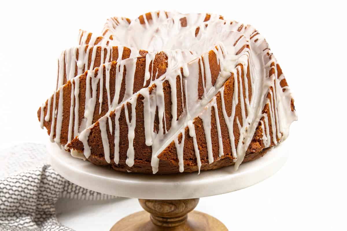 A ginger ale bundt cake with bourbon frosting on a marble cake stand.