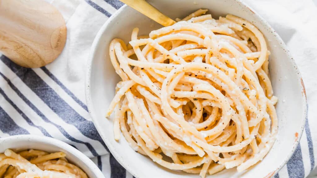 Bucatini cacio e pepe in a bowl with a gold fork and a pepper mill off to the side