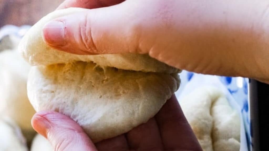 A steamed chinese bun with two hands pulling it apart.